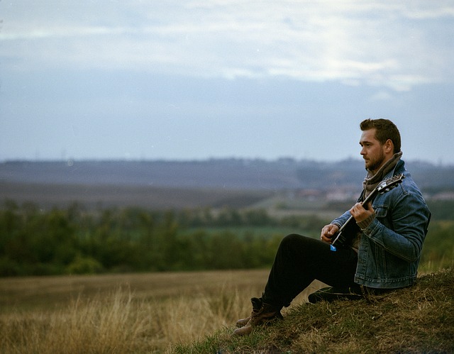 Junger Mann sitzt in der Natur und spielt Gitarre