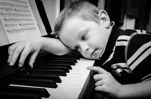 Klavier lernen für Anfänger Ein kleiner Junge spielt etwas traurig Klavier.